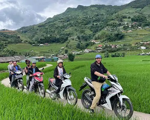 Riders on motorbikes pausing on a path between green Sapa rice fields
